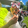 baby, child, headband, lollipop, hand, dress, white, outdoor, sunny, grass, golf_cart, people, trees, blue_sky, celebration, festive, person, summer, portrait, cute