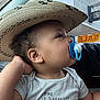 toddler, child, pacifier, hat, straw_hat, car_interior, window, raindrops, shirt, animal_print, sale_sign, side_profile, curly_hair, casual_clothing, hand, looking_away, indoors, daylight, cute, portrait