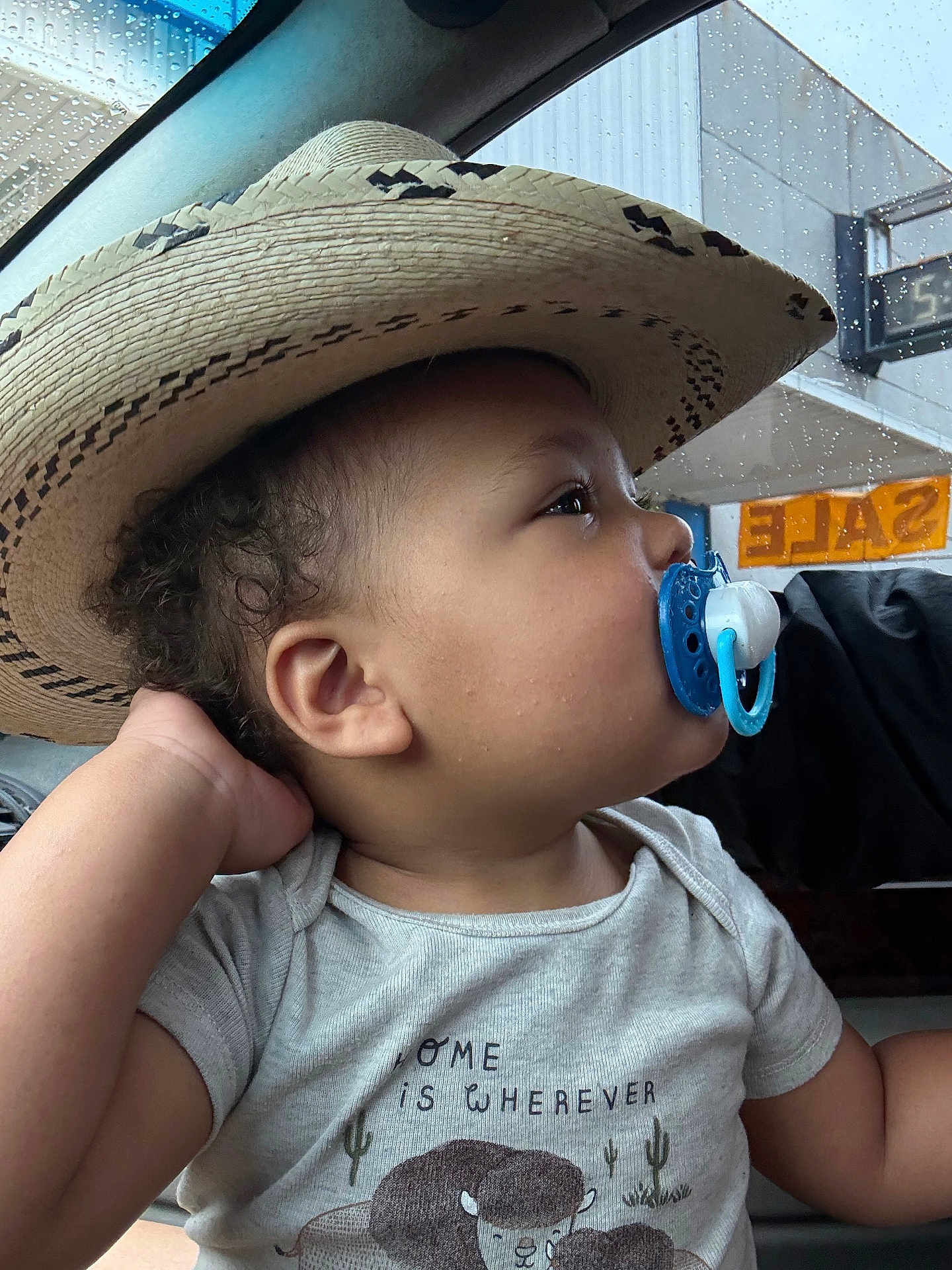 Amir joined the competition — help win amazing prizes! toddler, child, pacifier, hat, straw_hat, car_interior, window, raindrops, shirt, animal_print, sale_sign, side_profile, curly_hair, casual_clothing, hand, looking_away, indoors, daylight, cute, portrait