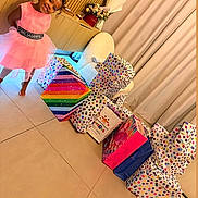 Anela is registered to the contest to win money with this photo: child, girl, smiling, pink_dress, indoor, gift_bags, presents, colorful, polka_dots, birthday, living_room, curtains, tile_floor, furniture, flowers, tissue_paper, portrait, standing, happy, social_media_screenshot