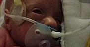 River is registered to the contest to win money with this photo: newborn, infant, baby, premature_baby, hospital, medical_tube, pacifier, swaddled, blanket, portrait, face, eyes_open, lying_down, close_up, indoor, bedding, healthcare, tiny, resting, photography