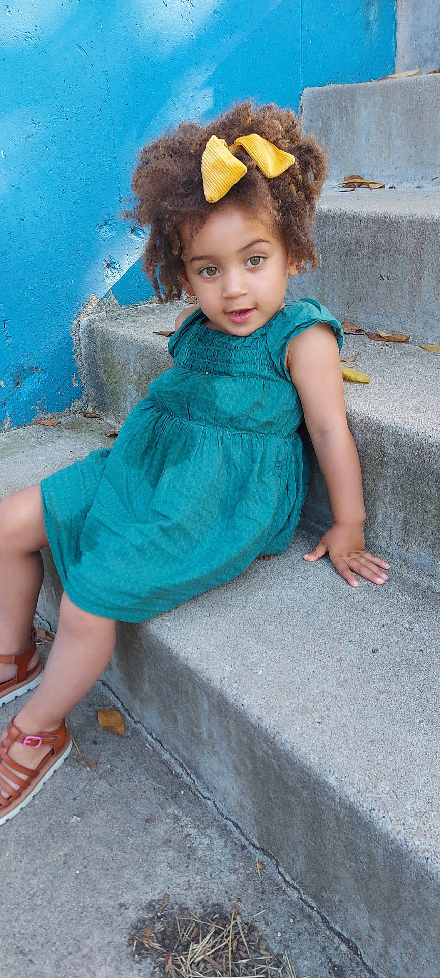 Ella is registered to the contest to win money with this photo: bodypart, child, clothing, dress, eveningdress, face, female, finger, footwear, formalwear, girl, happy, head, person, photography, portrait, sandal, shoe, sitting, smile