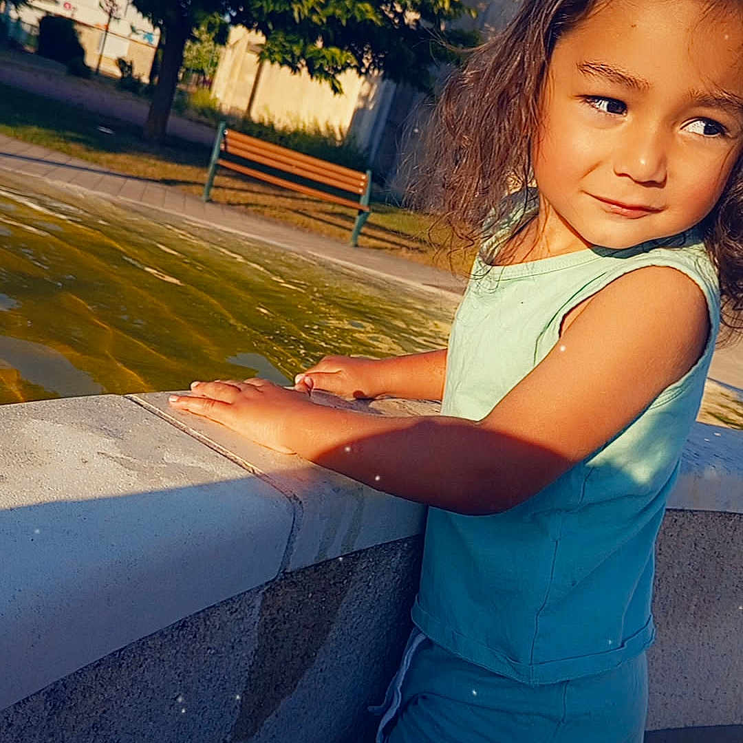 Anton participe au concours pour gagner de l'argent avec cette photo : bench, blue_shirt, blue_shorts, casual, child, curly_hair, daytime, kneeling, nature, outdoor, park, person, shadow, side_view, skin, summer_clothing, sunlight, thoughtful_expression, tree, water_fountain