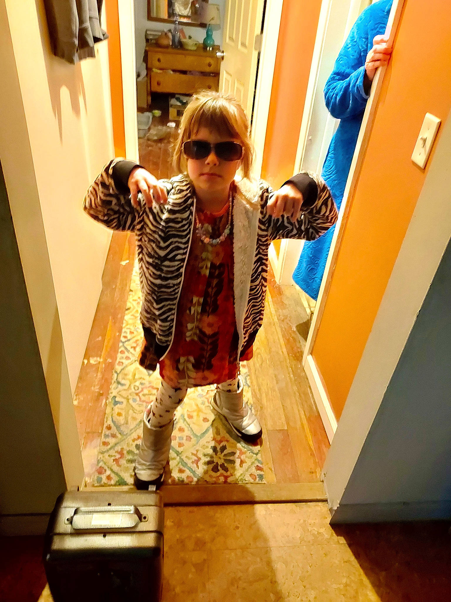 Talia is registered to the contest to win money with this photo: bag, door, eyewear, fashion_design, floor, flooring, fun, human_leg, joint, luggage_and_bags, pattern, person, room, shoulder, sleeve, standing, sunglasses, t_shirt, toddler, vision_care