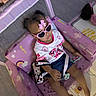 Tarranae is registered to the contest to win money with this photo: toddler, child, sunglasses, pink_bow, purple_couch, rainbow_pattern, toy_card, shorts, white_shirt, indoor, play_area, baby, childrens_furniture, pacifier, floor_mat, cute, relaxed, smiling, fashion, accessory
