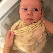 Léo a rejoint le concours — aidez-le/la à gagner de superbes lots ! baby, bath, blanket, child, closeup, expression, face, gentle, hands, indoors, infant, looking, person, portrait, skin, soft, tattoo, water, wrapped, yellow