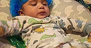 Dalen joined the competition — help win amazing prizes! baby, infant, child, portrait, lying_down, indoors, bed, pillow, blanket, dinosaur, onesie, blue_hat, clothing, pacifier, nursery, sleeping_area, face, baby_bedding, casual_photo, home