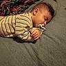 baby, bed, blanket, brown_hair, closed_eyes, colorful_blanket, cozy, curled_up, face, hand, indoors, infant, nap, pacifier, peaceful, portrait, resting, sleeping, soft_fabric, striped_clothing