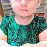 child, toddler, girl, portrait, close_up, face, smiling, wide_eyes, green_dress, hair_bow, earrings, sitting, hands, indoors, family, fashion, sparkly_clothing, cute, photography, headband