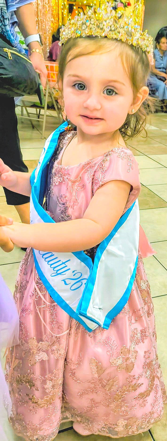 celebration, child, crown, decorations, fashion, formal_wear, girl, indoors, pageant, party, people, photography, pink_dress, portrait, sash, smiling, sparkles, standing, tile_floor, toddler