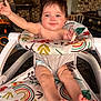 baby, infant, child, smiling, walker, highchair, diaper, legs, feet, arms, face, messy_face, food_on_face, patterned_fabric, rainbow_pattern, brick_wall, barbecue, outdoor, happy, seated