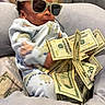 baby, child, infant, sunglasses, money, dollar_bills, cash, portrait, sitting, couch, blanket, onesie, indoor, close_up, face, hair, fashion, funny, relaxed, photography