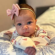 Arabella joined the competition — help win amazing prizes! baby, infant, headband, bow, cushion, pattern, hand, face, eyes, clothing, cute, portrait, indoor, child, expression, resting, soft, young, person, focus