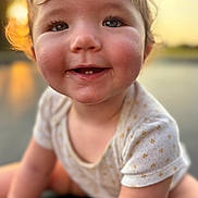 Paityn joined the competition — help win amazing prizes! baby, toddler, child, face, eyes, smile, teeth, drool, onesie, close_up, portrait, outdoors, sunset, bokeh, warm_light, cheeks, curly_hair, eyelashes, happy, candid