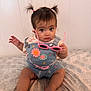baby, child, denim_overall, pigtails, pink_sunglasses, sitting, indoor, curious_expression, patterned_bedspread, embroidered_flowers, short_sleeves, cute, person, infant, legs, hand, wall, light_skin, brown_hair, clothing