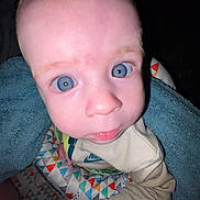 Paxton joined the competition — help win amazing prizes! baby, close_up, blue_eyes, towel, patterned_blanket, beige_clothing, nike_logo, infant, curious_expression, indoor, child, face, portrait, wide_eyes, young_child, skin, sitting, colorful, blanket, cute