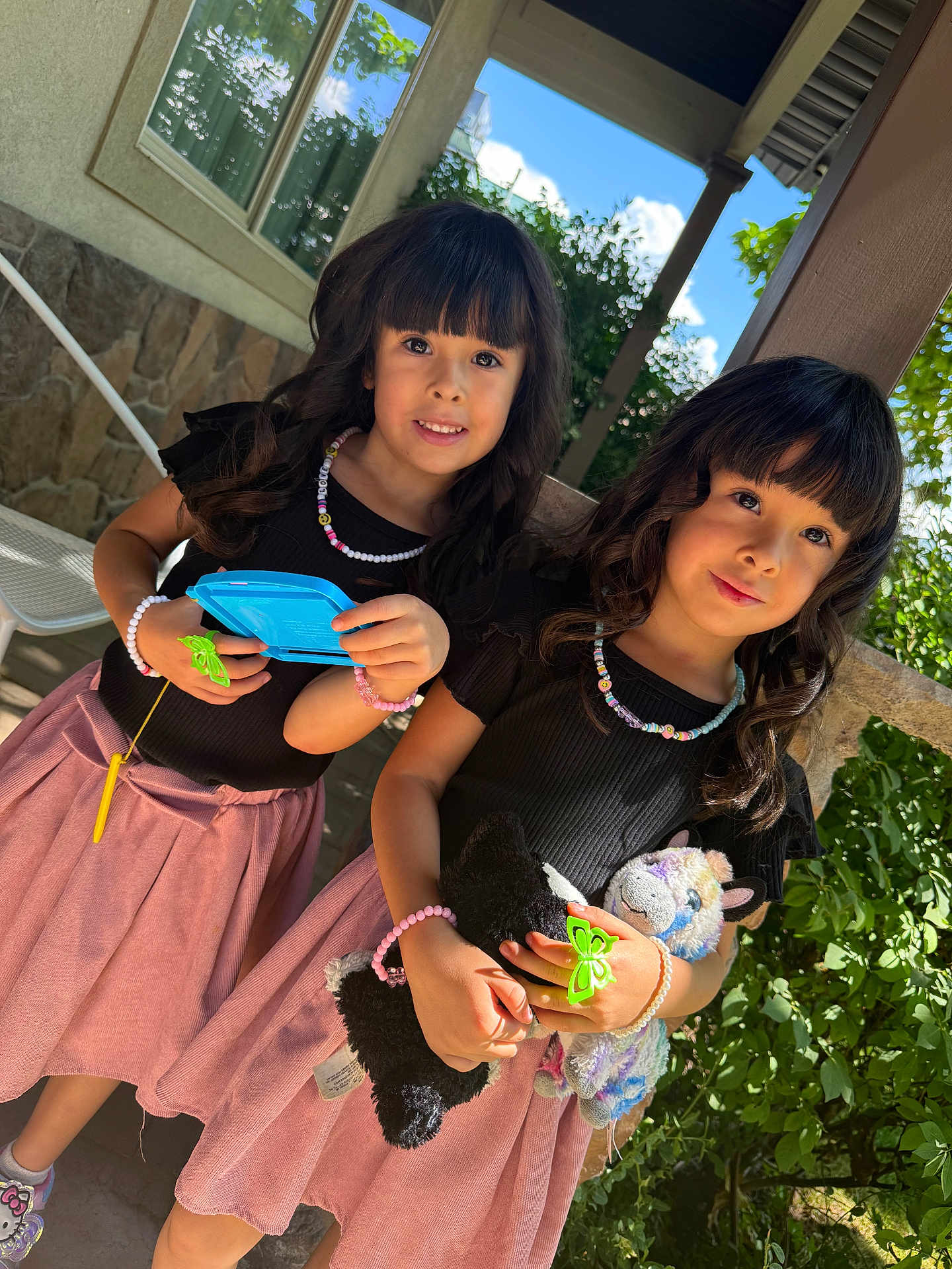 Ashley Y Grace joined the competition — help win amazing prizes! child, girl, outdoor, smile, toy, black_top, pink_skirt, bracelet, necklace, curly_hair, greenery, sunlight, stone_wall, porch, playful, cute, holding, friendship, happy, portrait