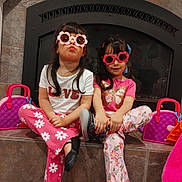 Ashley Y Grace joined the competition — help win amazing prizes! child, girl, sunglasses, pink, flower_shaped, pants, sitting, fireplace, indoor, toy_purse, fashion, cute, playful, portrait, casual_clothing, footwear, hair_accessory, smile, crossed_legs, toddler