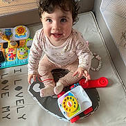 Héléna a rejoint le concours — aidez-le/la à gagner de superbes lots ! baby, child, childrens_toy, colorful_toys, curly_hair, cute, face, happy, indoors, infant, musical_toy, pink_pajamas, play_mat, playpen, playtime, sitting, smiling, sock, soft_lighting, toy_phone