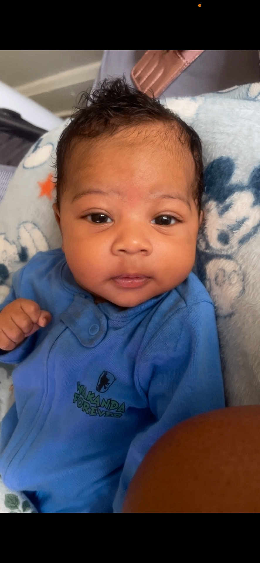 Ajani is registered to the contest to win money with this photo: baby, infant, blue_onesie, face, eyes, hand, blanket, soft, cute, newborn, portrait, indoors, clothing, expression, person, child, cozy, black_hair, skin, lying_down