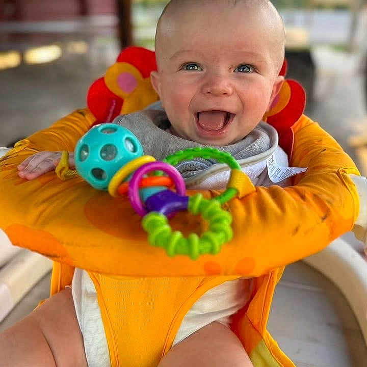 James Baby Jam is registered to the contest to win money with this photo: baby, baby_seat, blue_eyes, cheerful, child, chubby_legs, close_up, colorful_toys, cute, face, happy, indoor, infant, joyful, orange_seat, playful, portrait, sitting, smiling, toy