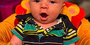 James Baby Jam is registered to the contest to win money with this photo: baby, child, infant, face, expression, striped_shirt, polo_shirt, orange_cushion, seat, indoors, blurred_background, wide_eyes, open_mouth, short_hair, cute, sitting, colorful_clothing, young_child, portrait, soft_lighting