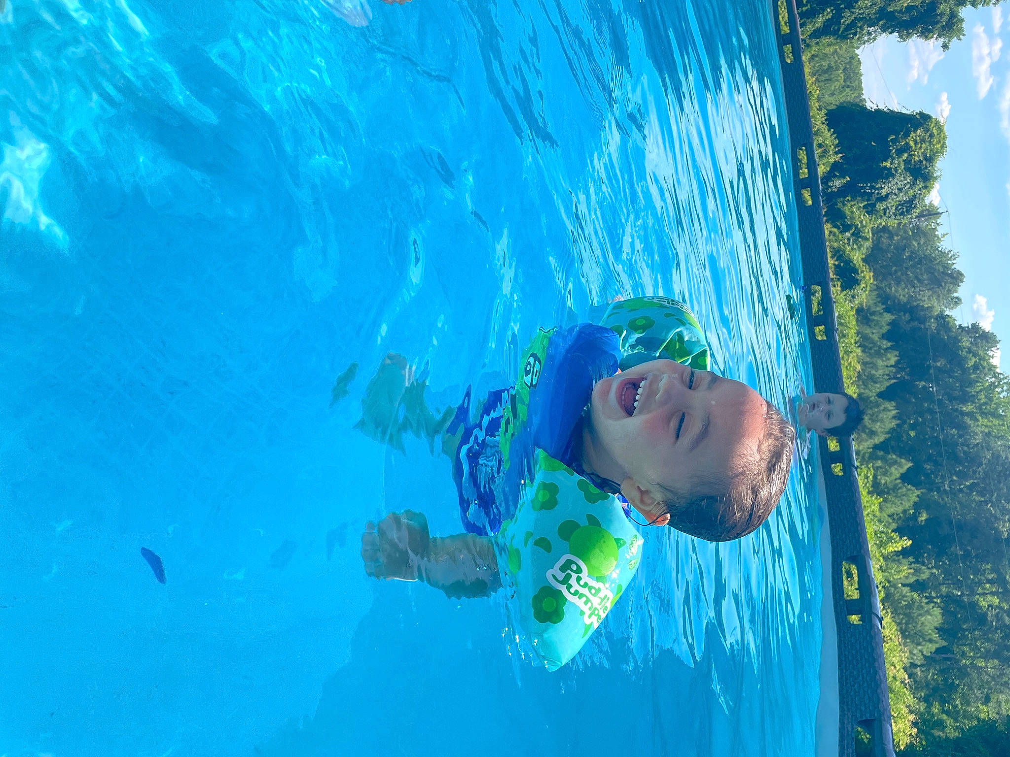 Rosa is registered to the contest to win money with this photo: azure, body_of_water, cloud, electric_blue, fun, happy, leisure, outdoor_recreation, people_in_nature, person, personal_protective_equipment, recreation, sky, smile, swimmer, swimming_pool, swimwear, toddler, tree, underwater