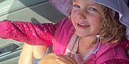 Arabella is registered to the contest to win money with this photo: child, girl, hat, pink_jacket, sequins, smile, sunlight, car_seat, car_interior, window, legs, sitting, casual_clothing, happy, outdoor_light, nature_background, footwear, shorts, portrait, daylight