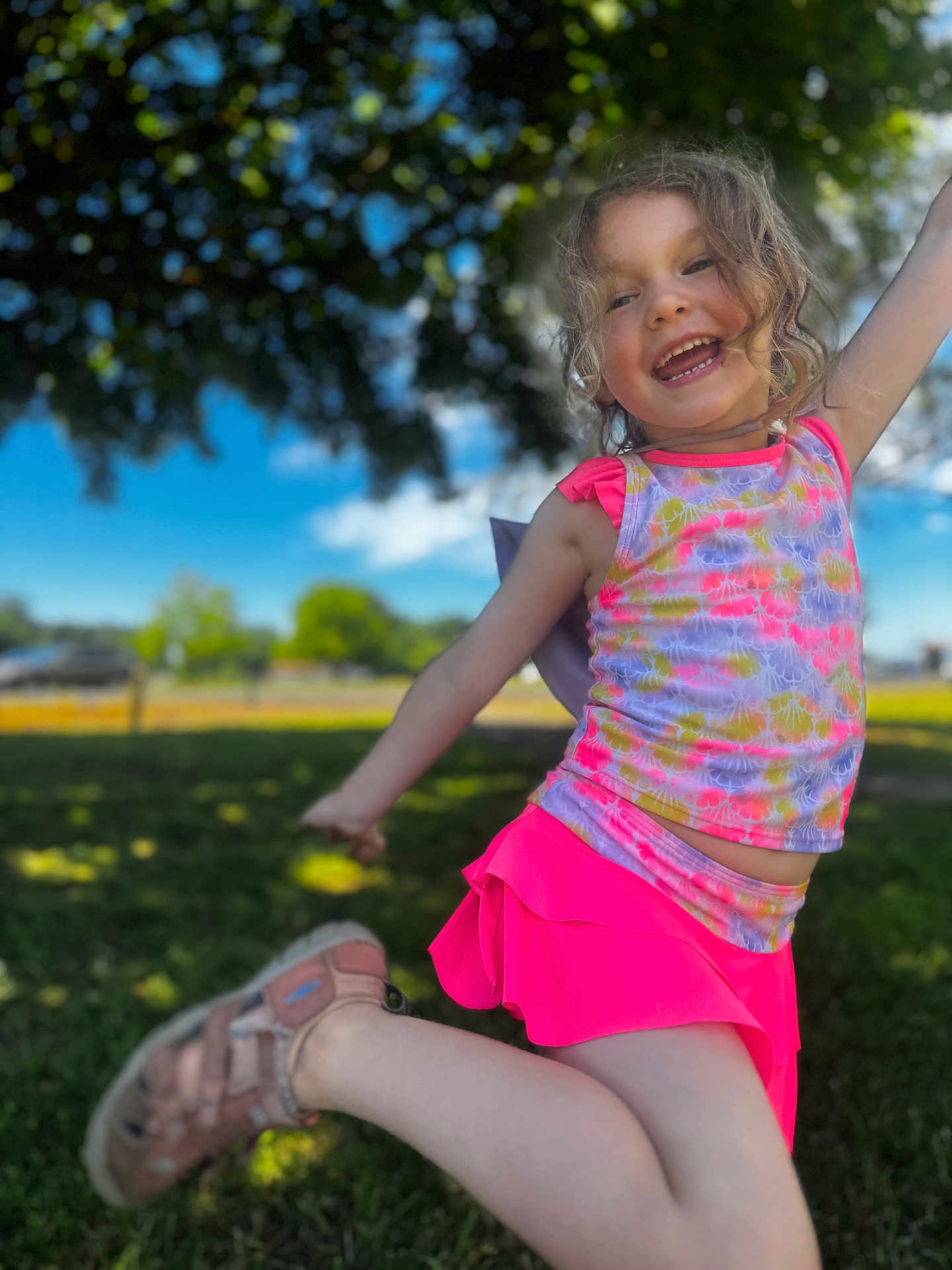 Arabella joined the competition — help win amazing prizes! child, girl, smiling, jumping, outdoor, daylight, grass, tree, blue_sky, curly_hair, pink_skirt, colorful_top, footwear, happy, playful, nature, sunlight, park, person, motion