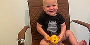 Jasper joined the competition — help win amazing prizes! toddler, child, smiling, chair, toy, yellow, black_clothing, indoor, floor, wall, happy, person, seat, furniture, cute, baby, sitting, foot, hand, expression