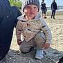 Jasper is registered to the contest to win money with this photo: toddler, child, beanie, hat, jacket, sweatpants, shoes, dinosaur_print, sand, beach, outdoor, daylight, water, people, background, nature, trees, sky, curious, crouching