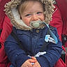 Léon participe au concours pour gagner de l'argent avec cette photo : toddler, child, stroller, pacifier, hooded_jacket, blue_eyes, toy, red_stroller, winter_clothing, cute, outdoor, baby, clothing, hands, seatbelt, portrait, young_child, casual_wear, warm, bundle