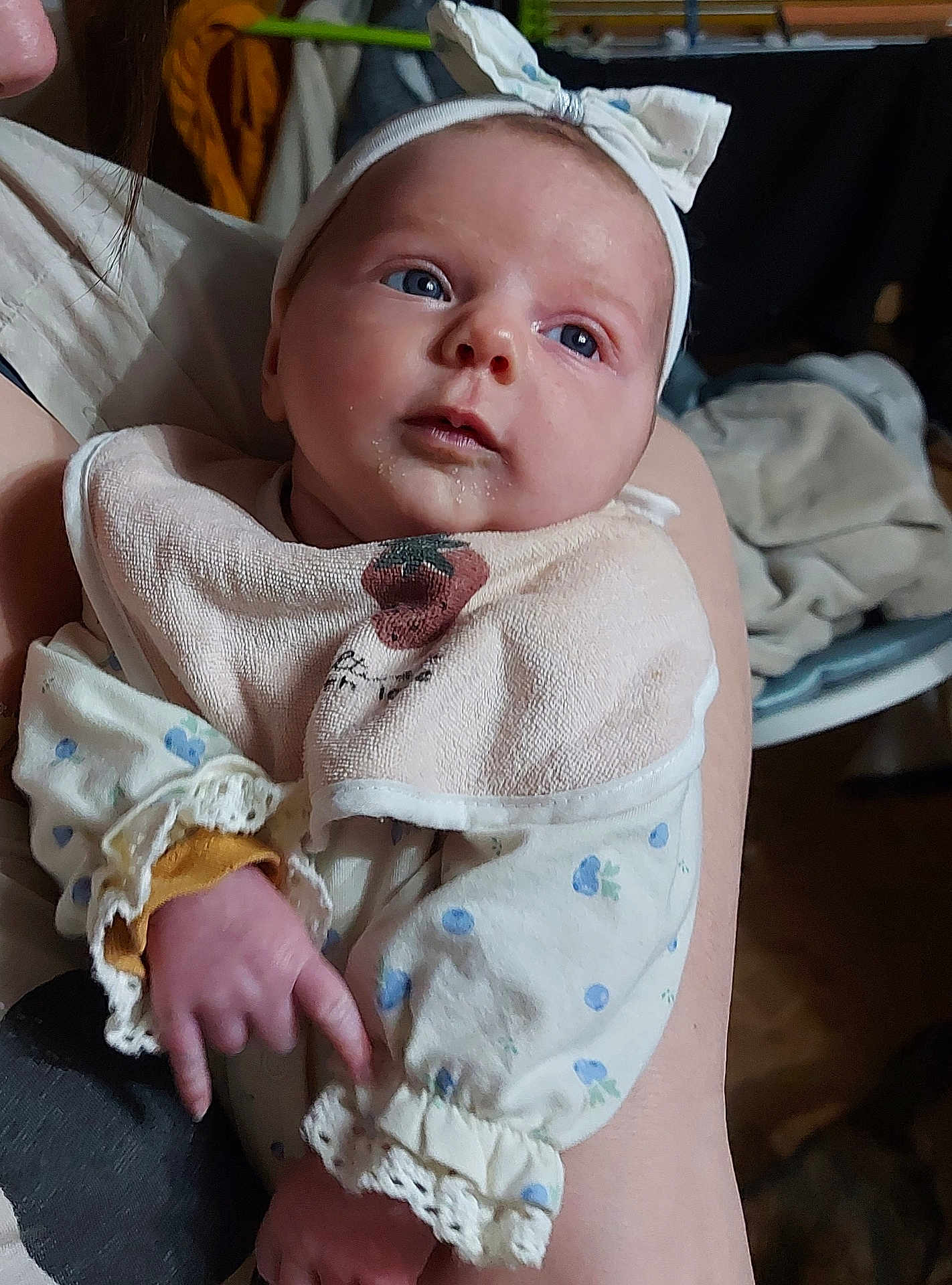 Mya a rejoint le concours — aidez-le/la à gagner de superbes lots ! baby, infant, newborn, headband, bib, blue_eyes, drool, hand, arm, lace_cuff, onesie, pattern, person, portrait, indoor, caregiver, blanket, bokeh_background, cozy, closeup