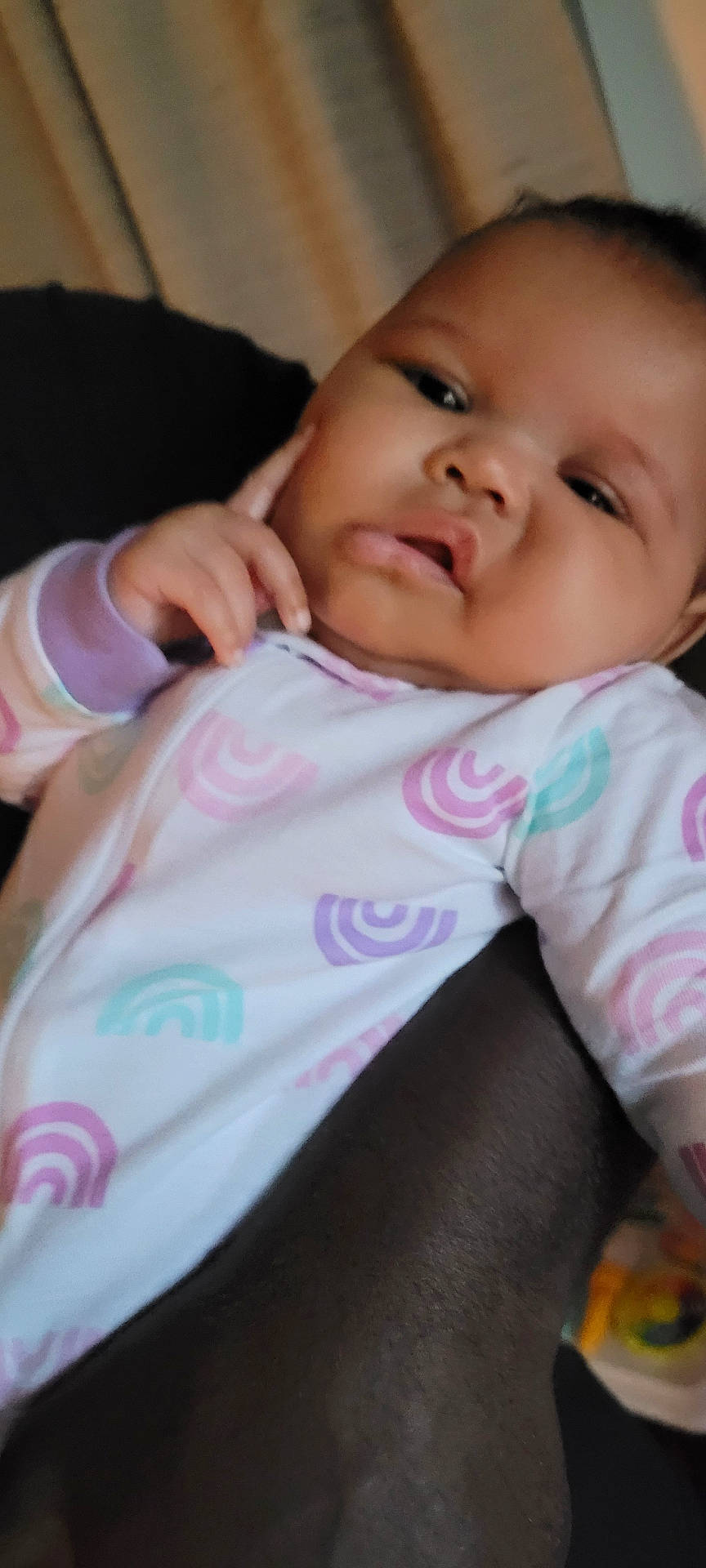 Serenity is registered to the contest to win money with this photo: adorable, baby, child, close_up, clothing, couch, curious, eyes, face, finger, hand, head, indoor, infant, onesie, photography, portrait, rainbow_pattern, seated, serious