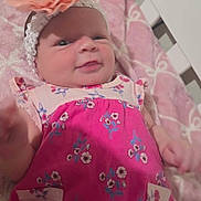 Chloe is registered to the contest to win money with this photo: baby, infant, crib, blanket, headband, flower, pink_clothing, floral_pattern, smile, face, child, indoors, furniture, bed, cute, newborn, lying_down, person, soft_toys, cozy