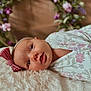 baby, infant, face, headband, flower, floral_pattern, blanket, soft_texture, cute, lying_down, portrait, indoor, child, closeup, pink, white, decor, young, peaceful, adorable