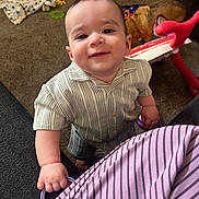 Theodore is registered to the contest to win money with this photo: baby, child, smiling, indoor, carpet, toy, dog, striped_clothing, hand, face, person, playful, crawling, home, furniture, background, pet, floor, blanket, colorful