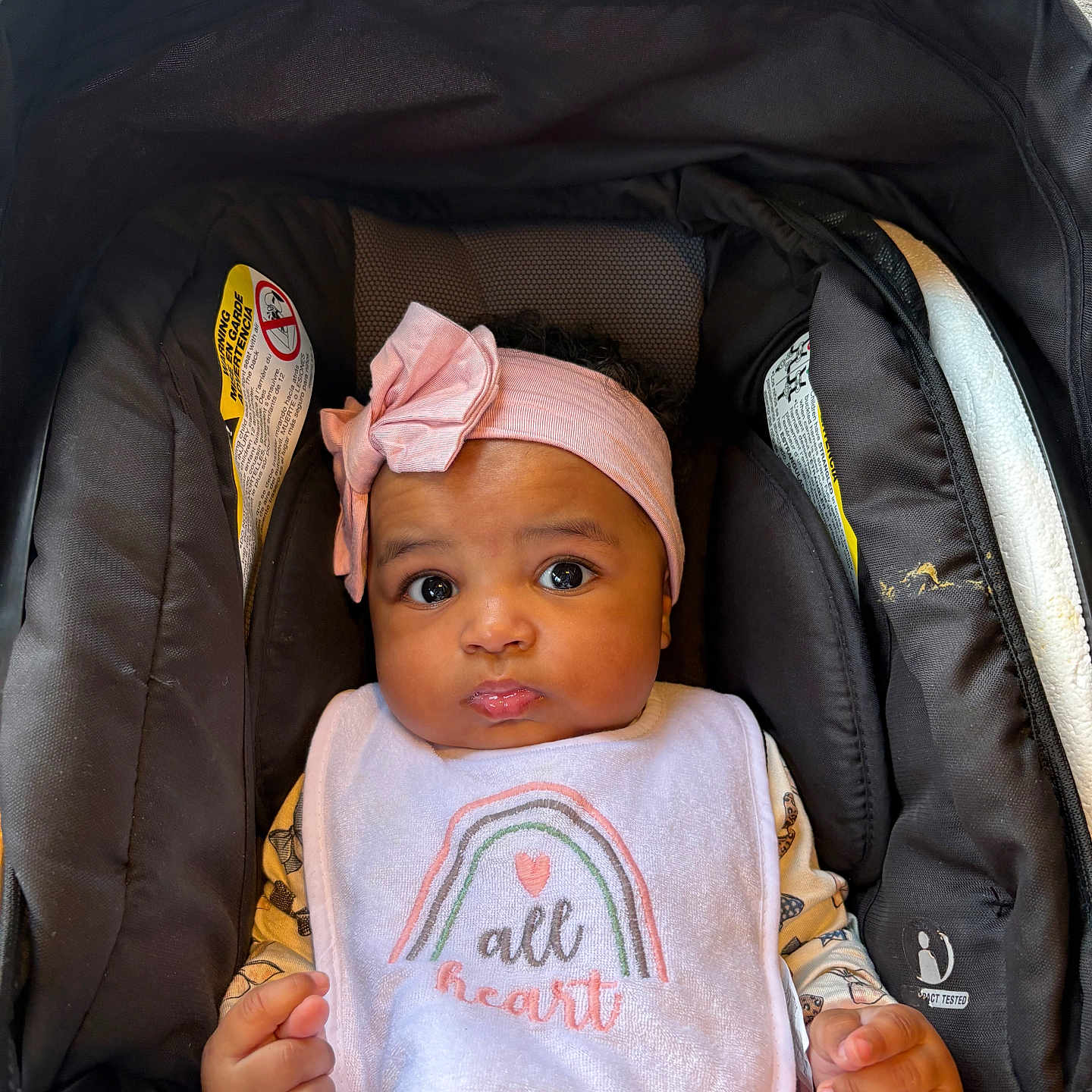Jurzi joined the competition — help win amazing prizes! baby, child, car_seat, headband, bib, pink, clothing, infant, cute, portrait, sitting, indoor, face, hands, expression, seatbelt, black, fabric, person, closeup
