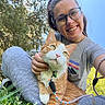 Butter is registered to the contest to win money with this photo: person, cat, glasses, outdoor, grass, tree, blue_sky, leash, smile, casual_clothing, orange_cat, white_cat, happy, nature, sunlight, sitting, pet, closeup, daylight, playful
