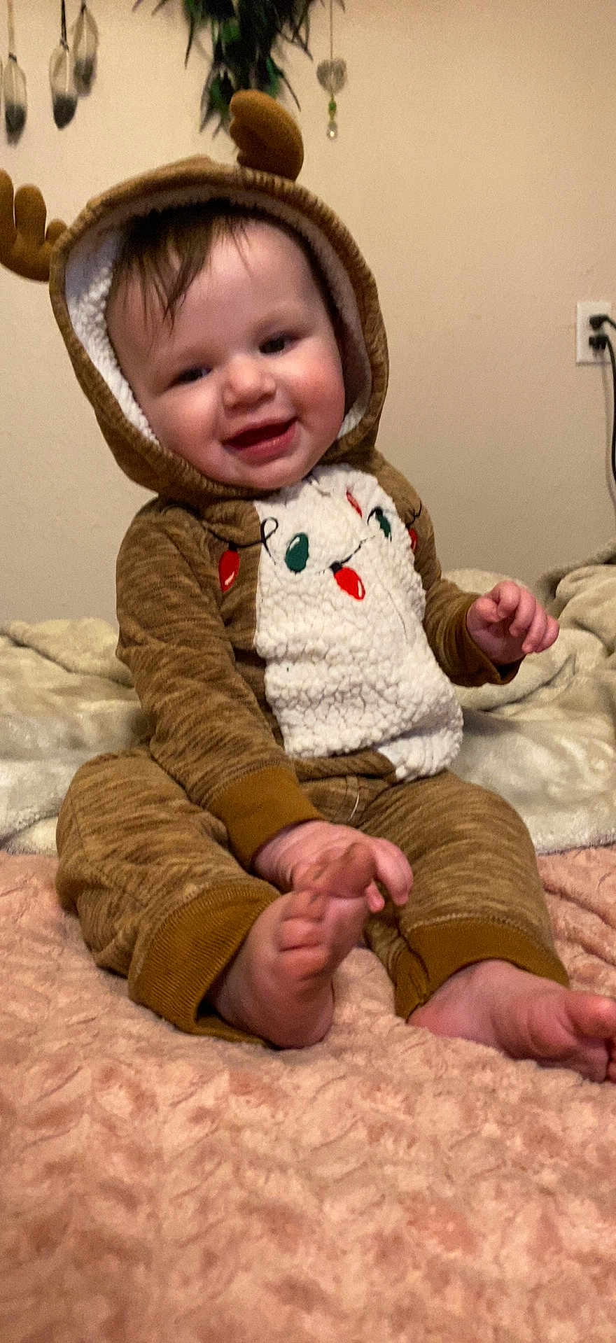 Amethyst Jade is registered to the contest to win money with this photo: baby, child, smiling, reindeer_costume, onesie, antlers, blanket, indoor, cute, happy, face, feet, hand, wall, power_outlet, soft_texture, seated, infant, cozy, holiday