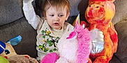 Kameron joined the competition — help win amazing prizes! toddler, child, stuffed_animal, unicorn, party_hat, couch, plush_toy, indoor, celebration, toy, bear, cozy, clothing, socks, curious, seated, soft_toy, living_room, wooden_wall, party