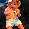 baby, child, smiling, orange_shirt, bucket_hat, mickey_mouse, shorts, sitting, couch, indoor, cute, happy, portrait, person, infant, headwear, furniture, expression, skin, clothing