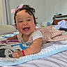 Greeicy is registered to the contest to win money with this photo: baby, smiling, curly_hair, pink_bow, lying_down, animal_mat, bedroom, happy, infant, cute, child, indoor, playtime, colorful, soft_lighting, portrait, toddler, clothing, fabric, cozy