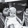 baby, man, child, black_and_white, kiss, family, portrait, love, outdoor, casual_clothing, beard, dress, holding, expression, person, blurred_background, affection, toddler, young_child, candid