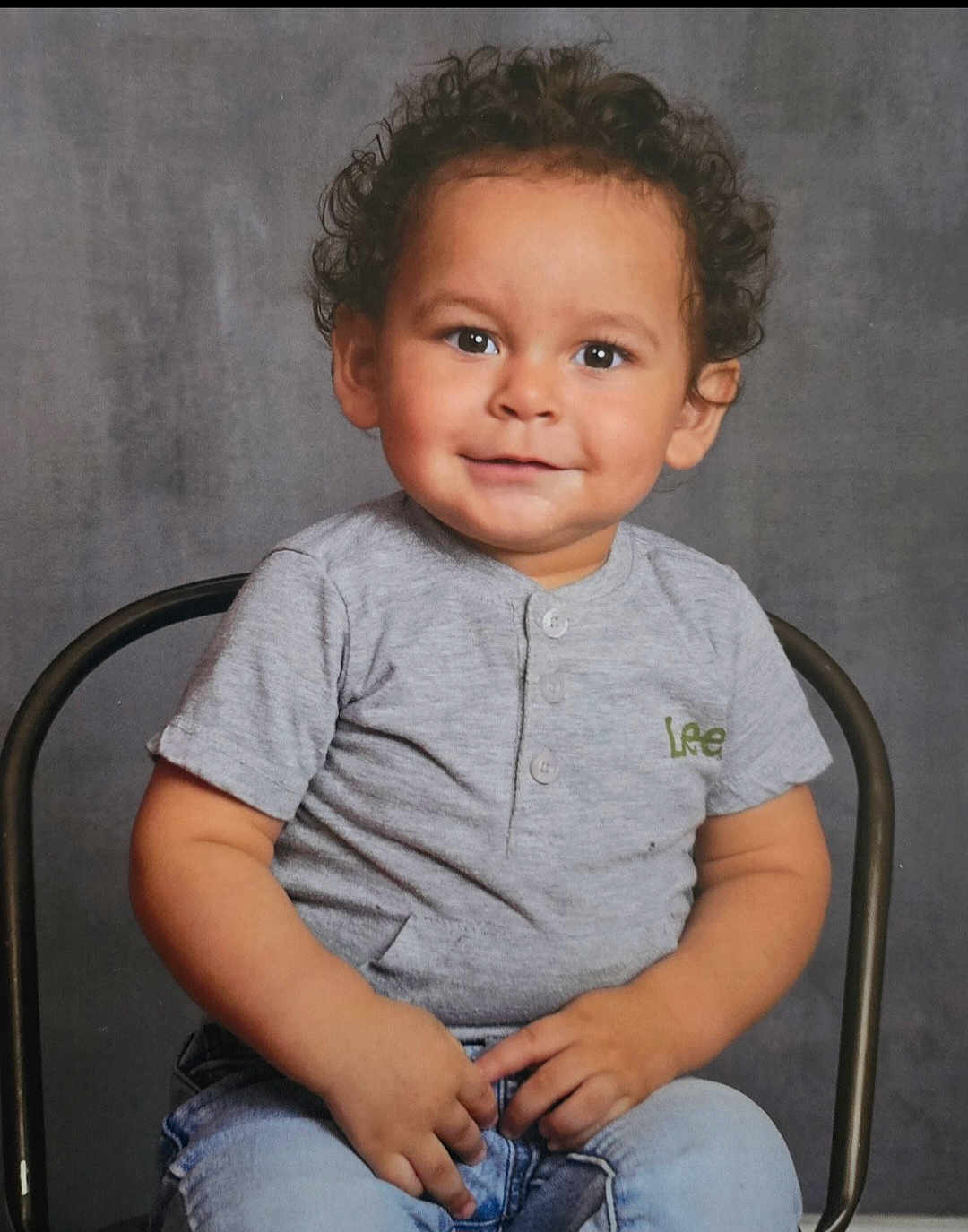 Jorge joined the competition — help win amazing prizes! child, toddler, smiling, curly_hair, grey_shirt, jeans, sitting, chair, portrait, casual_clothing, happy, cute, indoor, studio, young_child, person, face, expression, background, hands