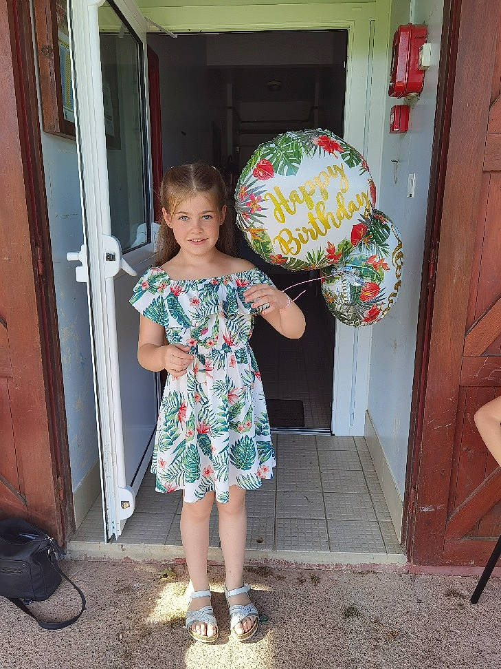 Zélie a rejoint le concours — aidez-le/la à gagner de superbes lots ! baby_toddler_clothing, balloon, child, door, dress, event, flooring, fun, happy, human_leg, joy, magenta, party_supply, pattern, person, pink, sandal, smile, standing, textile