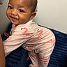 Emori joined the competition — help win amazing prizes! baby, child, smiling, onesie, flamingo_pattern, couch, blue_couch, hand, climbing, happy, cute, indoor, person, footed_pajamas, earring, skin, face, infant, closeup, portrait
