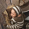 baby, sleeping, knitwear, striped_clothing, brown, white, pillow, blanket, hat, antennae, wooden_floor, rustic, cozy, infant, portrait, cute, indoors, resting, soft_texture, warm