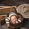 baby, newborn, sleeping, knitted_clothing, striped, bucket, wooden_props, hat, cozy, brown, white, infant, cute, resting, soft_texture, indoor, portrait, peaceful, baby_fashion, adorable