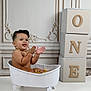 baby, child, bathtub, clawfoot_tub, orange_slices, clapping, happy, smiling, gold_chain, decorative_wall, blocks, letters, one, indoor, studio, cute, playful, water, skin, portrait